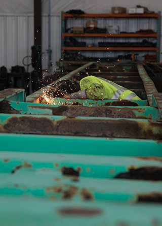 Worker welding green chassis with sparks flying