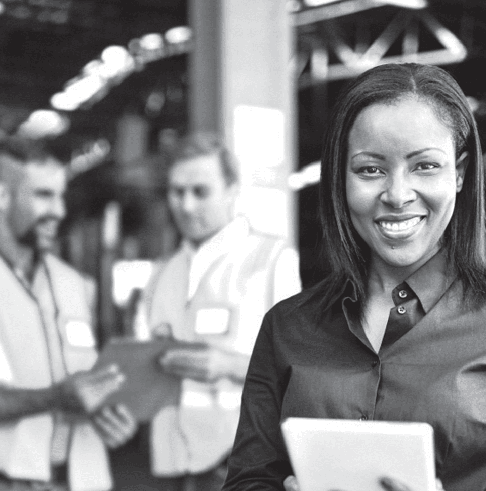 Business woman smiling standing in front of two male workers looking at a clipboard