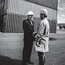 Two terminal workers in front of stacked shipping containers shaking hands